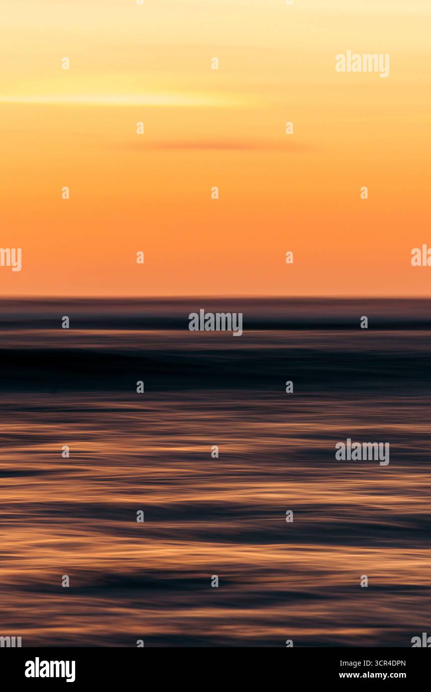 Verschwommener Sonnenuntergang über Meereswellen mit leuchtenden Orange- und Dunkeltönen. Krui, Lampung, Sumatra, Indonesien Stockfoto