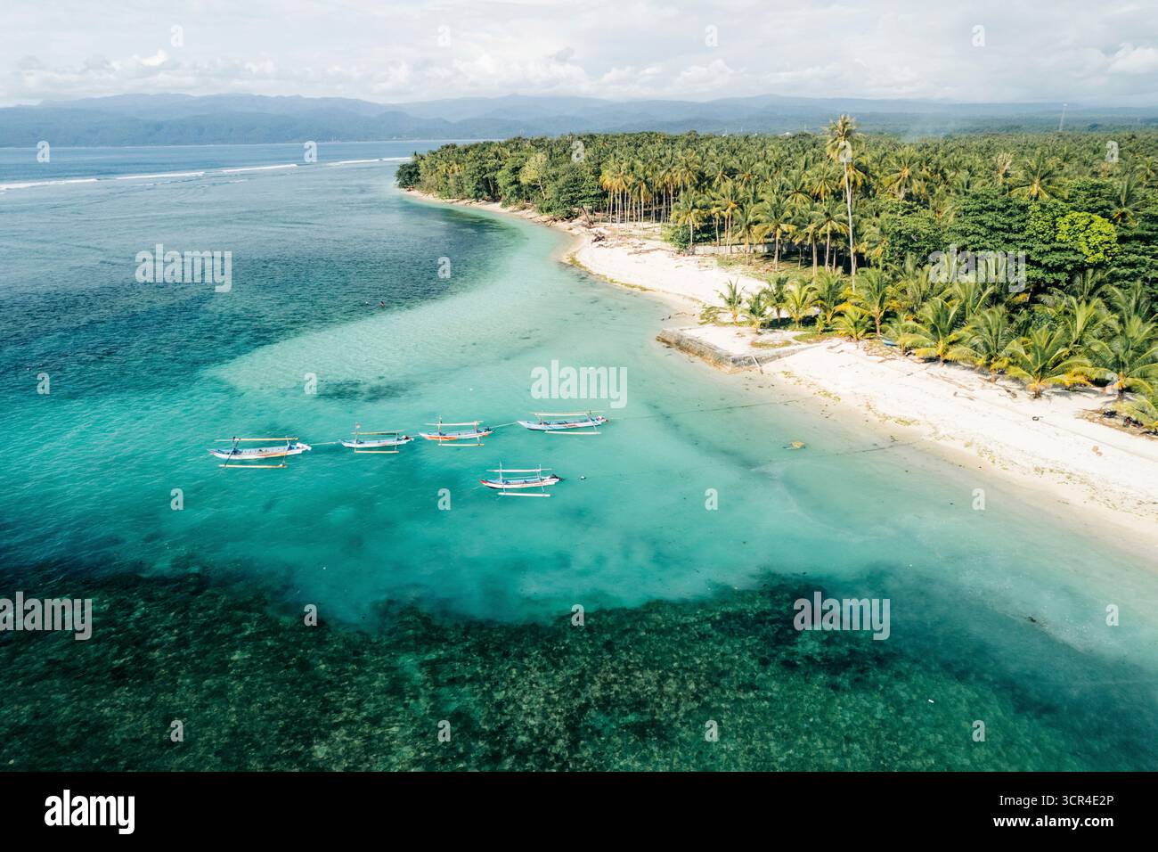 Blick aus der Vogelperspektive auf traditionelle Boote im klaren türkisfarbenen Meer in der Nähe eines Sandstrandes. Krui-Küste in Lampung, Indonesien Stockfoto