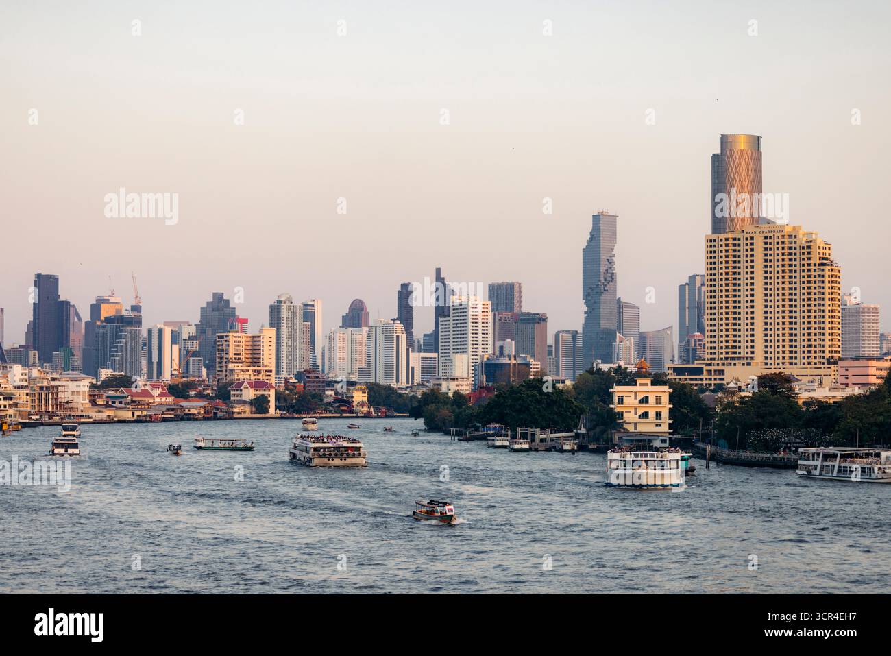 Skyline der Stadt mit Wolkenkratzern und Booten auf einem breiten Fluss bei Sonnenuntergang. Chao Phraya River, Bangkok, Thailand Stockfoto