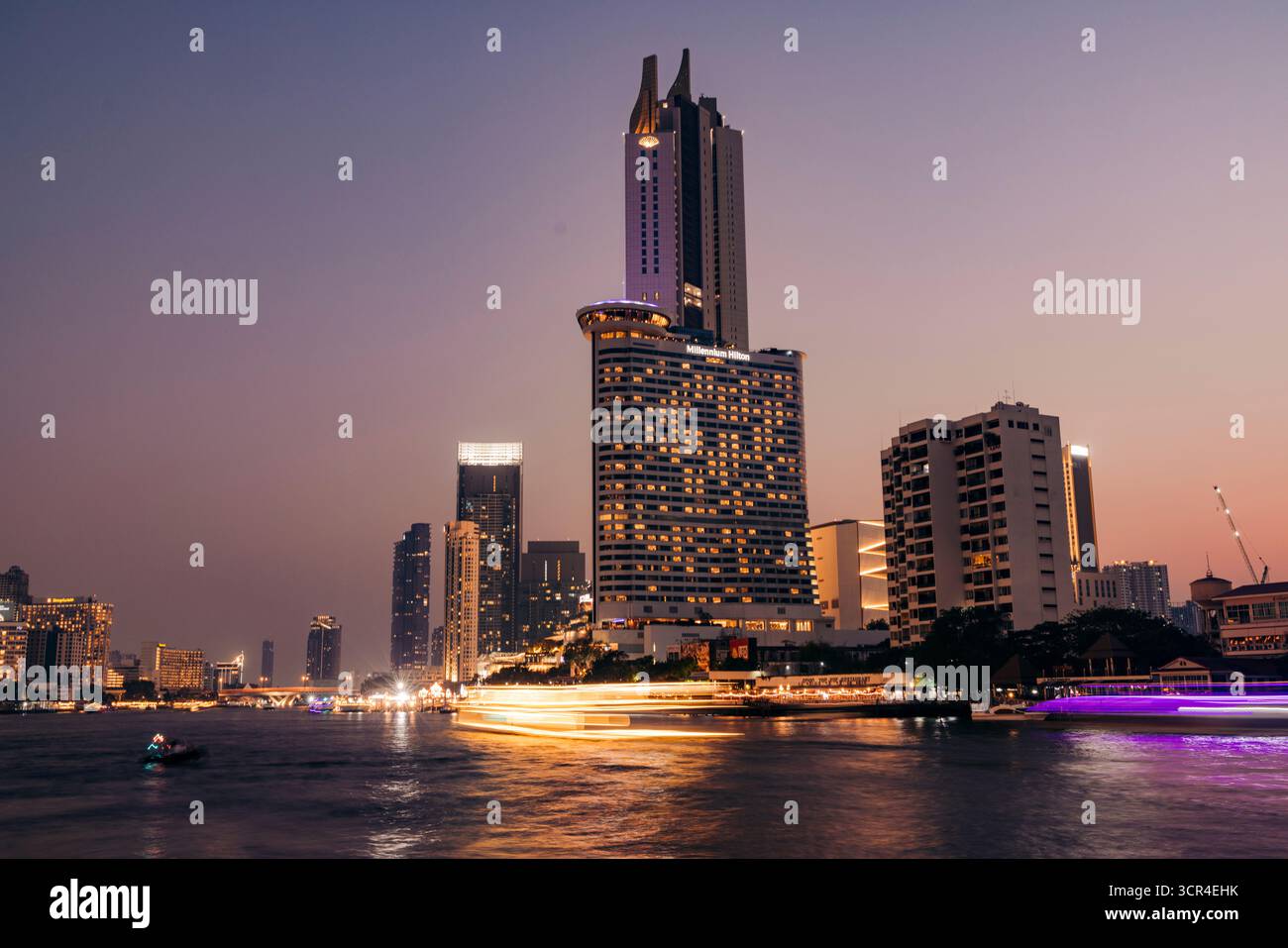 Hohe moderne Wolkenkratzer überragen in der Dämmerung einen belebten Fluss mit lebendigen Lichtern der Stadt. Chao Phraya River, Bangkok, Thailand Stockfoto