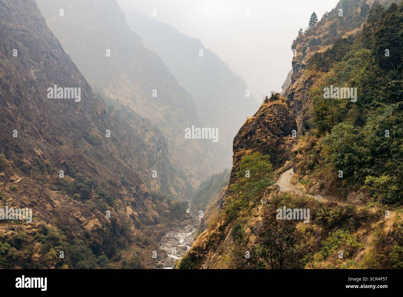 Nebliges Bergtal mit zerklüfteten Klippen und einem gewundenen, schmalen Pfad entlang des Hügels. Straße F36 von Annapurna in der Provinz Gandaki, Nepal Stockfoto