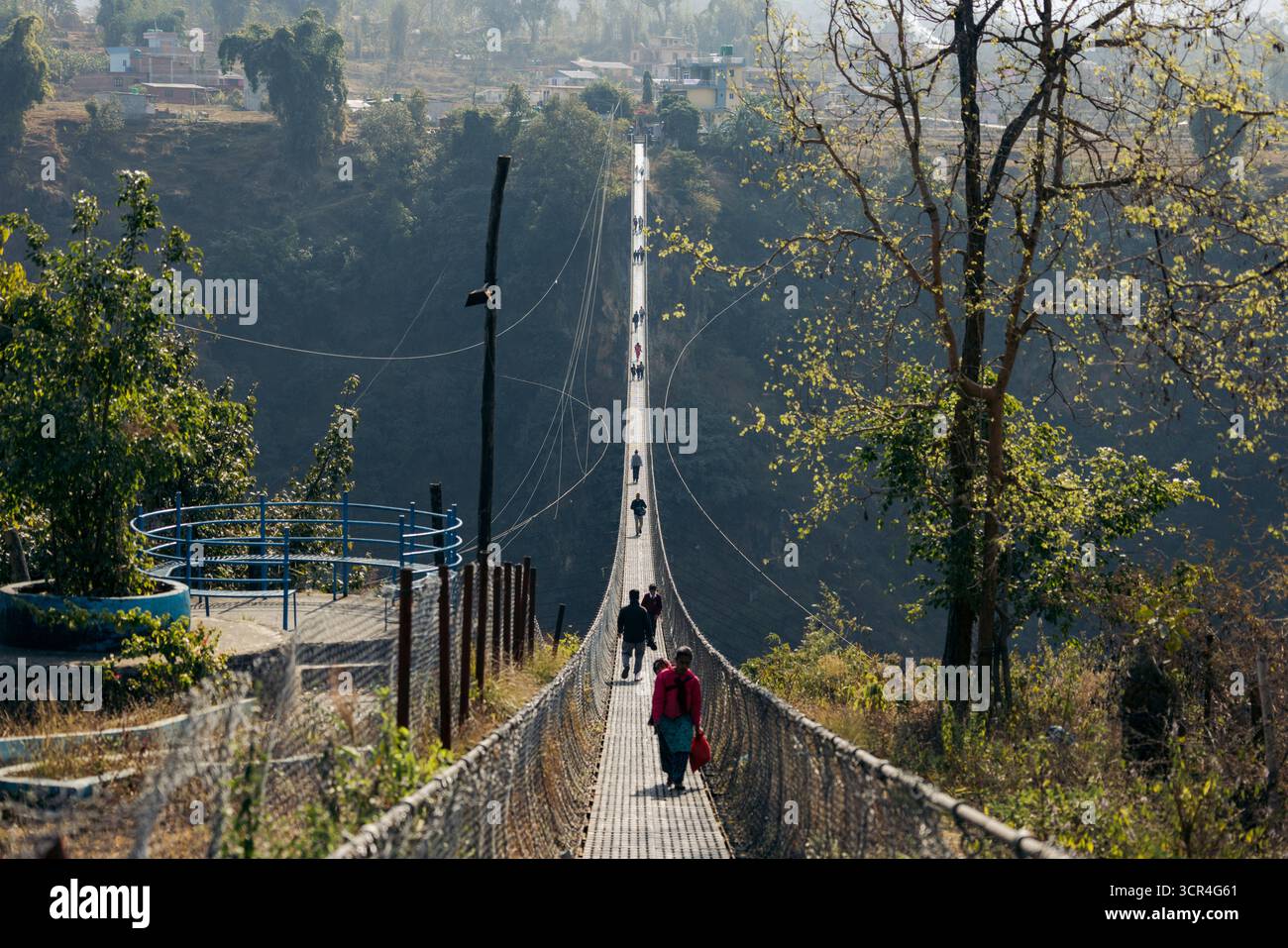 Menschen, die auf der Kushma Hängebrücke laufen, umgeben von üppigem Grün und fernen Hügeln. Kushma, Bezirk Parbat, Provinz Gandaki, Nepal Stockfoto