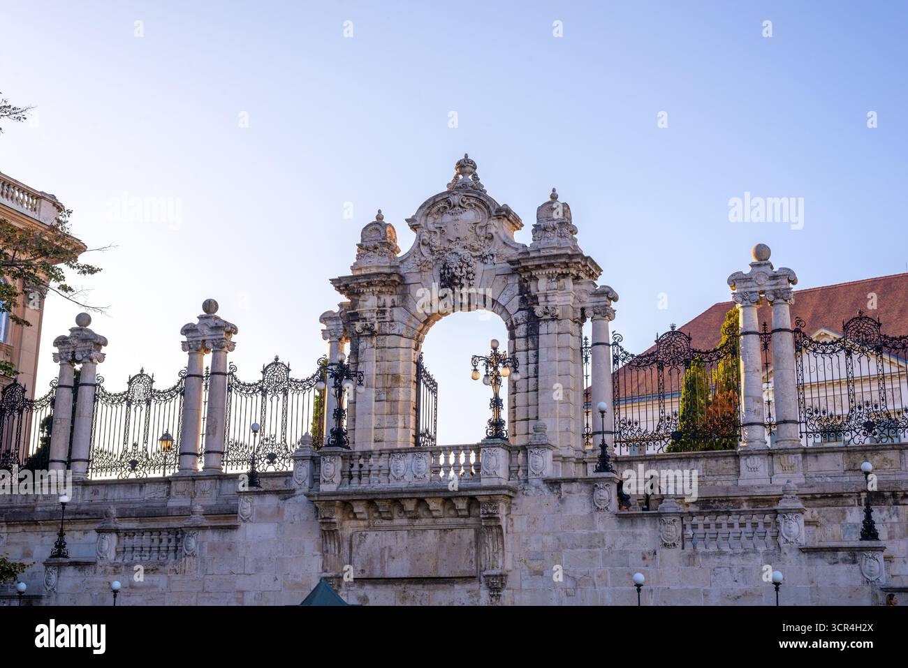 Historisches barockes Eingangstor der Burg Buda mit raffinierten Details, Steinskulpturen und eisernen Geländern unter klarem blauem Himmel Stockfoto