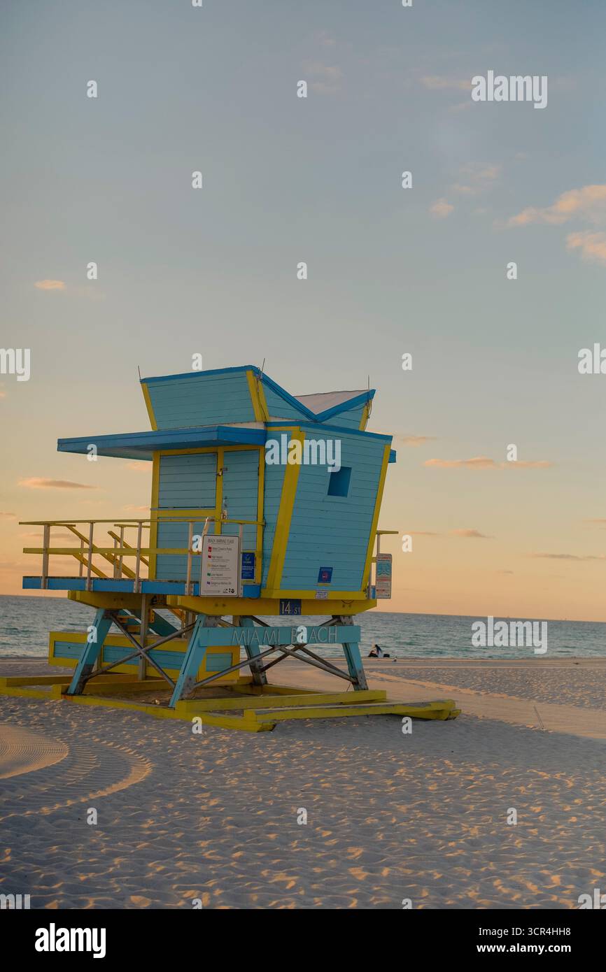 Ein farbenfroher Rettungsschwimmer-Turm an einem ruhigen Strand bei Sonnenuntergang, der lange Schatten auf den Sand wirft. Miami, Florida, USA Stockfoto