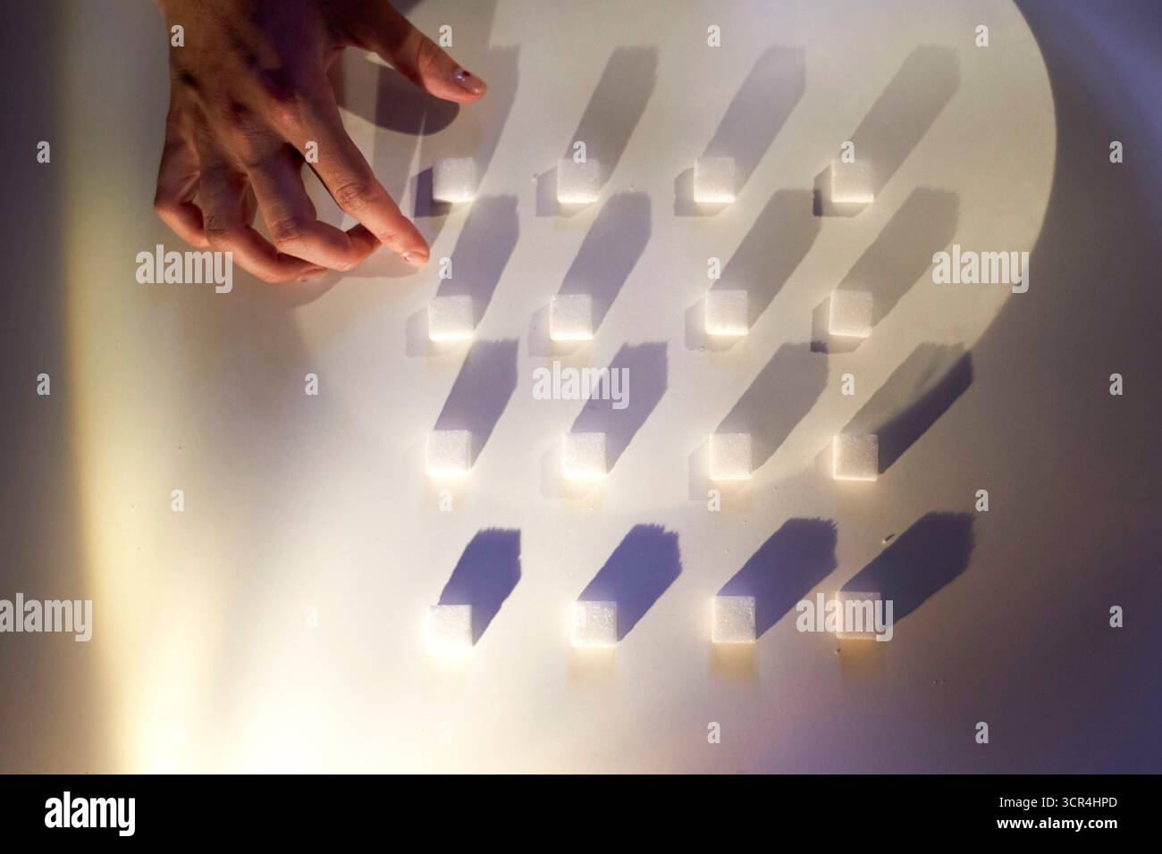 Zuckerschwürfel von Hand auf einer weißen Oberfläche mit dramatischen Schatten anordnen. Stockfoto