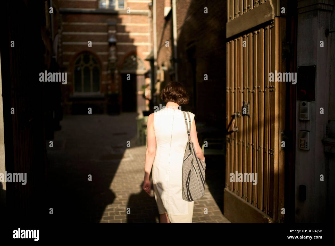 Frau in einer sonnendurchfluteten Gasse mit einer Tasche, in einem ärmellosen weißen Kleid. Deutschland Stockfoto