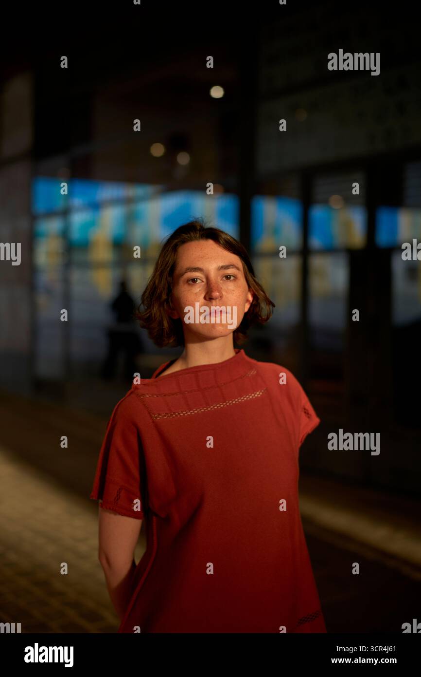 Eine Frau in rotem Kleid steht unter warmen Lichtern auf einer kopfsteingepflasterten Straße. Brüssel, Belgien Stockfoto