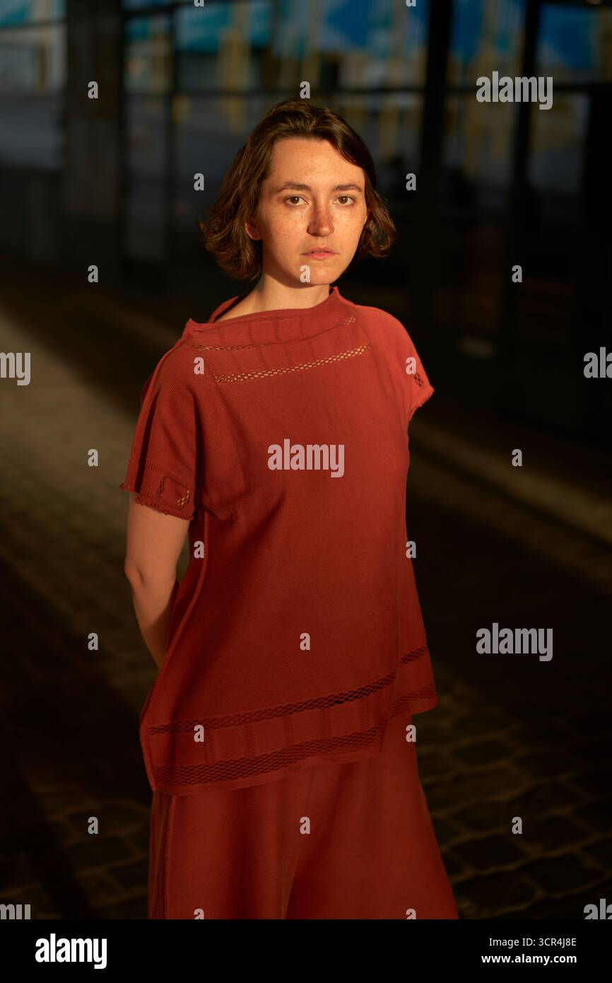 Eine Frau in rotem Kleid steht unter warmen Lichtern auf einer kopfsteingepflasterten Straße. Brüssel, Belgien Stockfoto