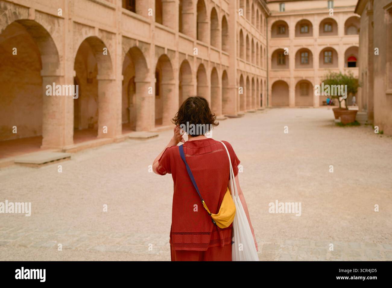 Frau in rotem Outfit geht durch einen historischen Innenhof mit Bögen und sanfter Beleuchtung. Marseille, Frankreich Stockfoto