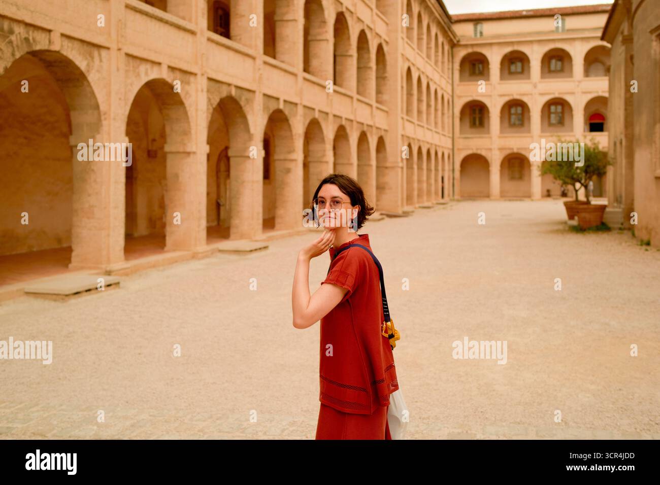 Frau in rotem Kleid, die durch einen historischen Steinhof mit Bögen und Säulen geht. Marseille, Frankreich Stockfoto