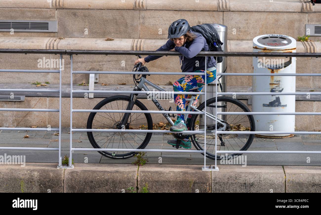 Eine junge Frau, die auf einem Fahrrad sitzt und sich auf Eisengeländer stützt, scheint tief in Gedanken zu sein Stockfoto