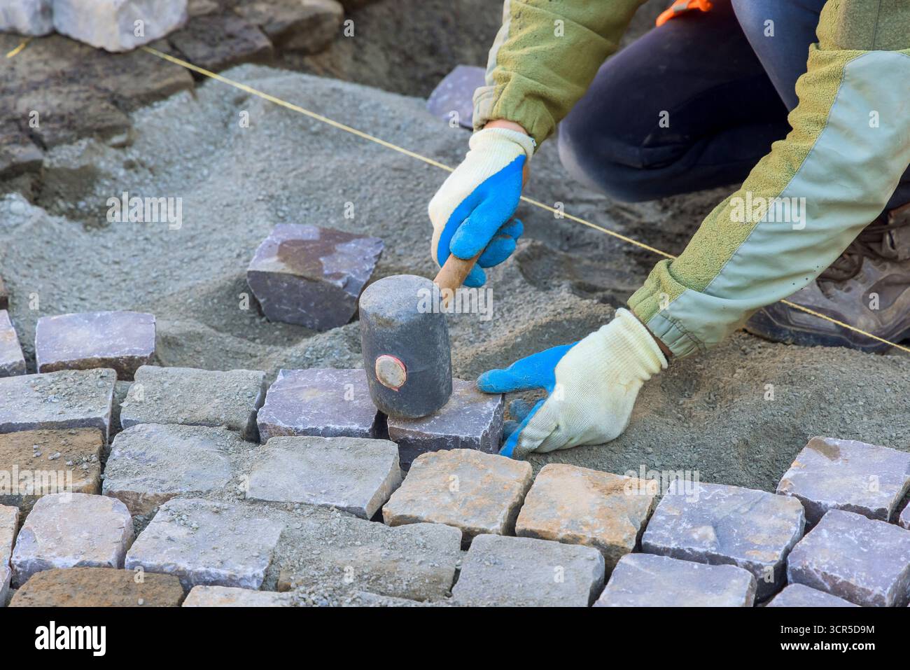 Der Arbeiter legt am Arbeitstag auf der Baustelle sorgfältig Pflastersteine und Sand für den neuen Weg ab. Stockfoto