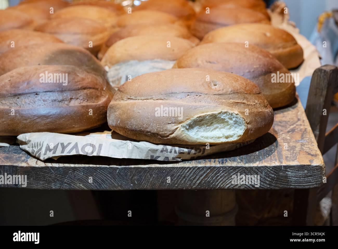 Kreta, Griechenland. Frisch gebackene warme Brotlaibe mit weißem rundem, knusprigem Brot, das auf einem Holztisch in einer Bäckerei gekühlt wird. Stockfoto