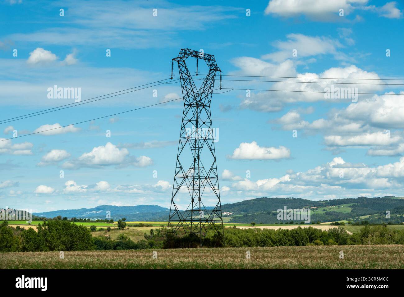 Hochspannungsleitungen gegen einen hellblauen Himmel mit verstreuten Wolken, Puy de Dome, Auvergne Rhone Alpes, Frankreich Stockfoto