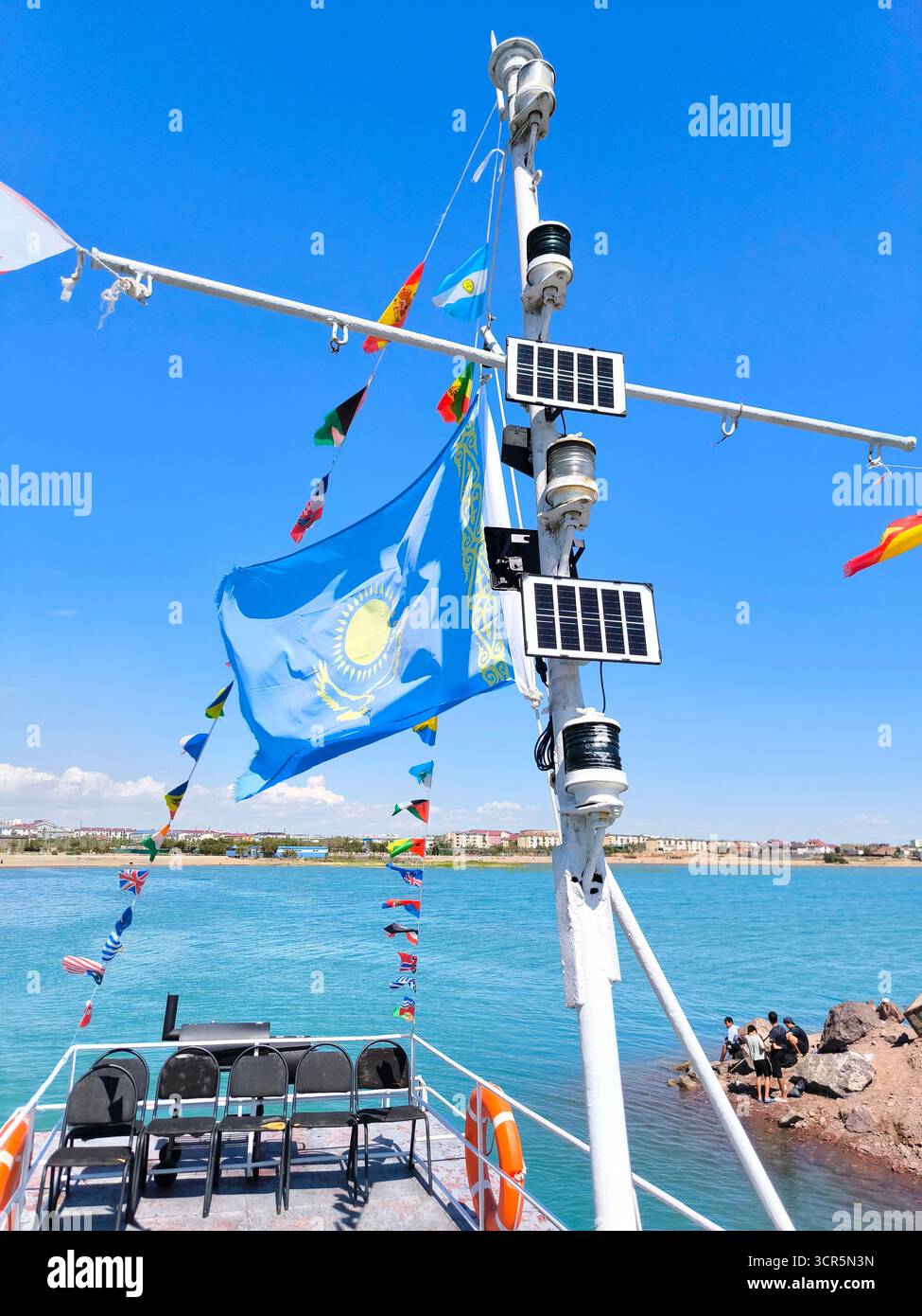 Von einem Boot aus haben Sie einen Blick auf den wunderschönen Balchash-See in Kasachstan an einem klaren, sonnigen Tag. Eine große, helle Nationalflagge Kasachstans flattert im Vorbild Stockfoto