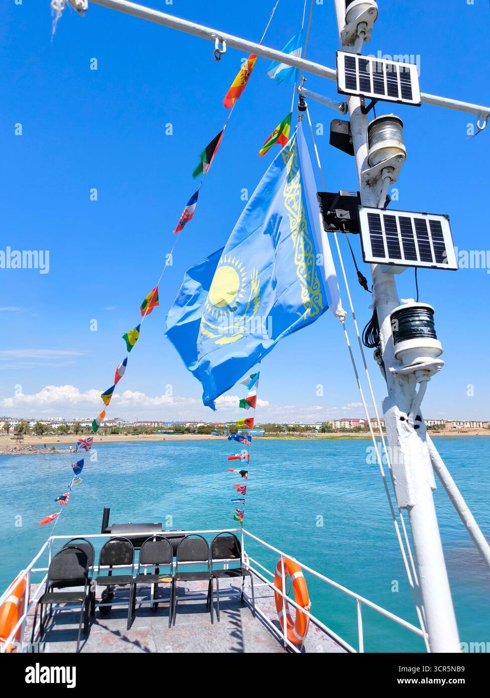 Von einem Boot aus haben Sie einen Blick auf den wunderschönen Balchash-See in Kasachstan an einem klaren, sonnigen Tag. Eine große, helle Nationalflagge Kasachstans flattert im Vorbild Stockfoto