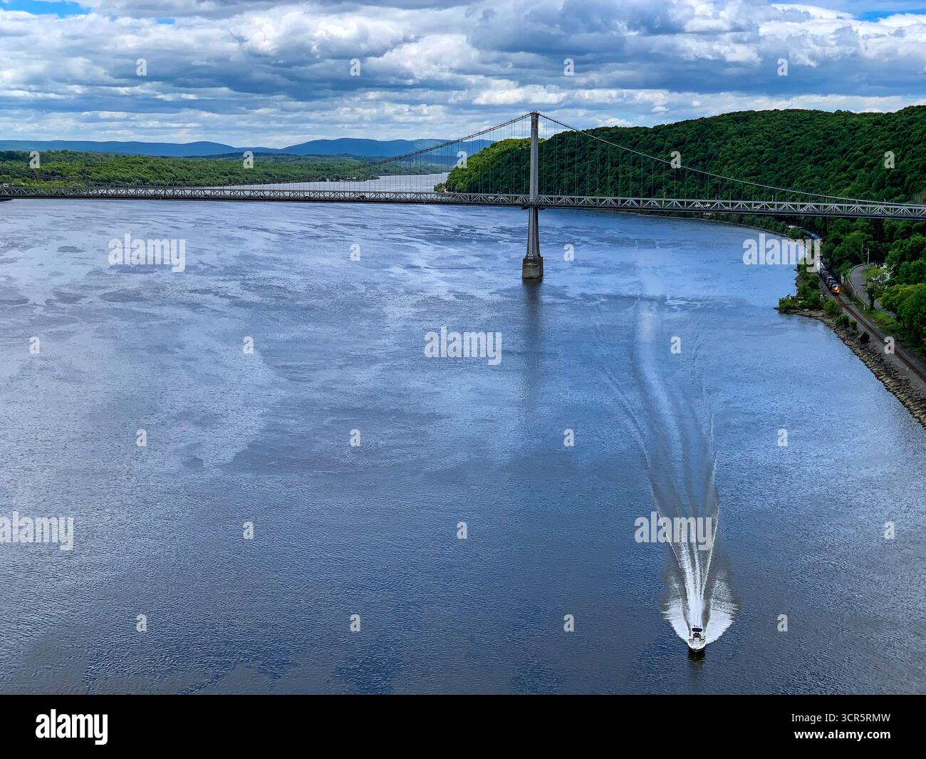 Aus der Vogelperspektive eines Bootes, das durch das dunkle, reflektierende Wasser in Richtung Mid-Hudson Bridge unter einem dramatischen Himmel schneidet, Poughkeepsie, New York, Vereinigte Staaten Stockfoto