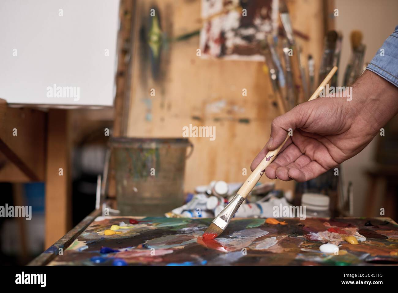Künstler, der im Studio arbeitet. Männliche Hand hält Pinsel und mischt Ölfarben auf bunter, unordentlicher Palette, Nahaufnahme Stockfoto