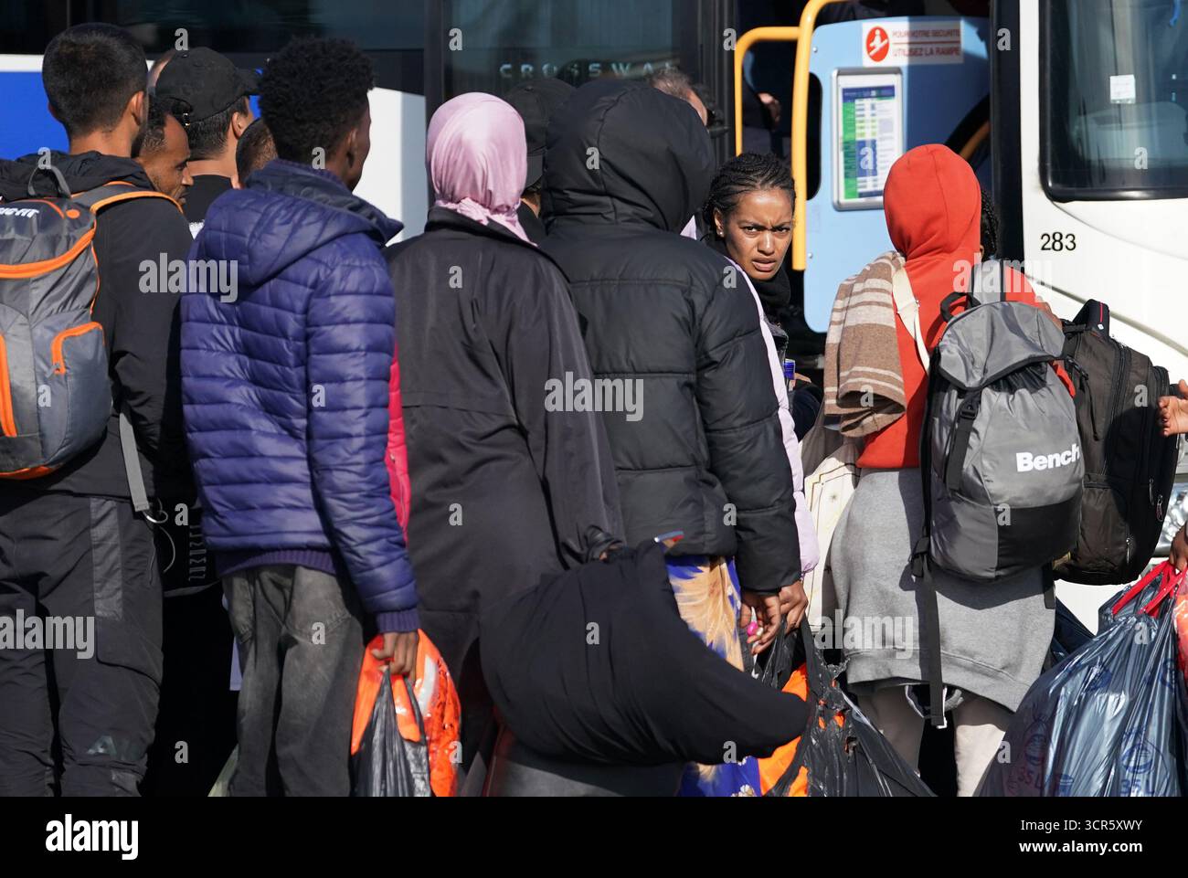 Menschen, die als Migranten gelten, halten ihre Sachen, während sie in Gravelines, Frankreich, an Bord eines lokalen Busses stehen. Bilddatum: Montag, 29. September 2025. Stockfoto