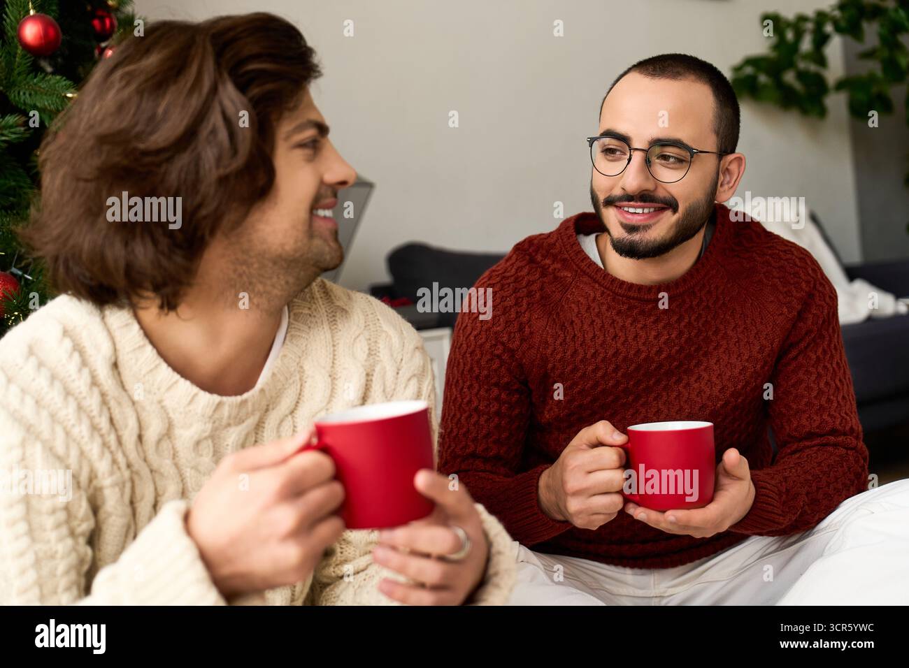 Das Paar genießt warme Getränke und lacht in ihrem fröhlichen Zuhause, während es den Feiertagsgeist feiert. Stockfoto
