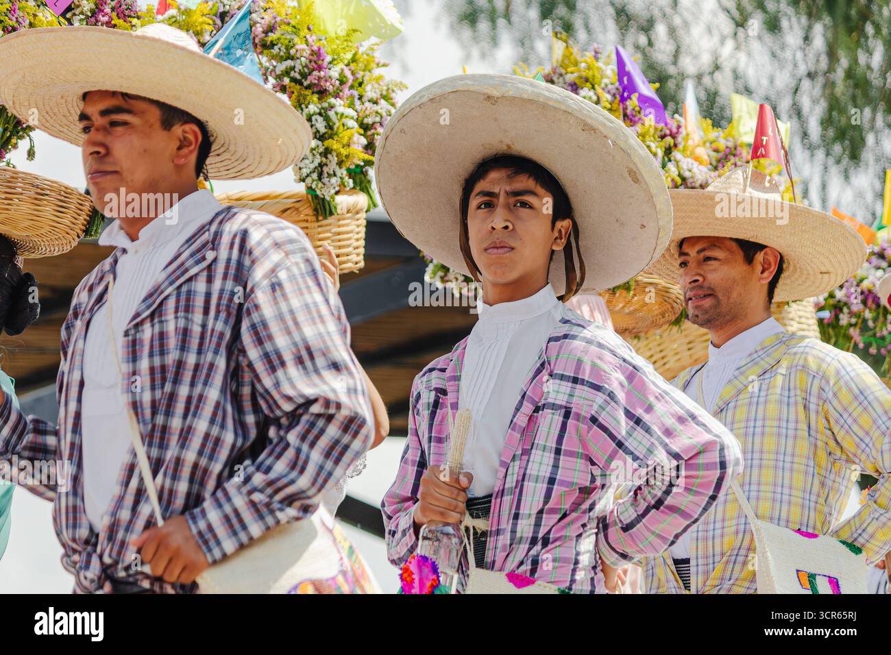 Männer mit Strohhüten und farbenfrohen karierten Hemden, glücklich und lächelnd, nehmen an einem traditionellen Tanz im Freien teil. Stockfoto