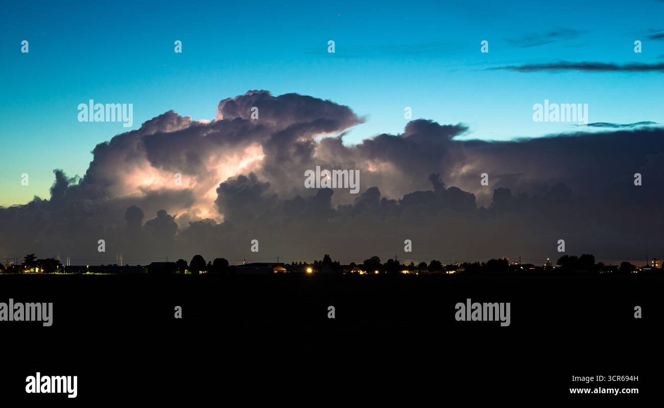 Entfernte Gewitterwolken werden in der Abenddämmerung durch Lichtblitze beleuchtet Stockfoto
