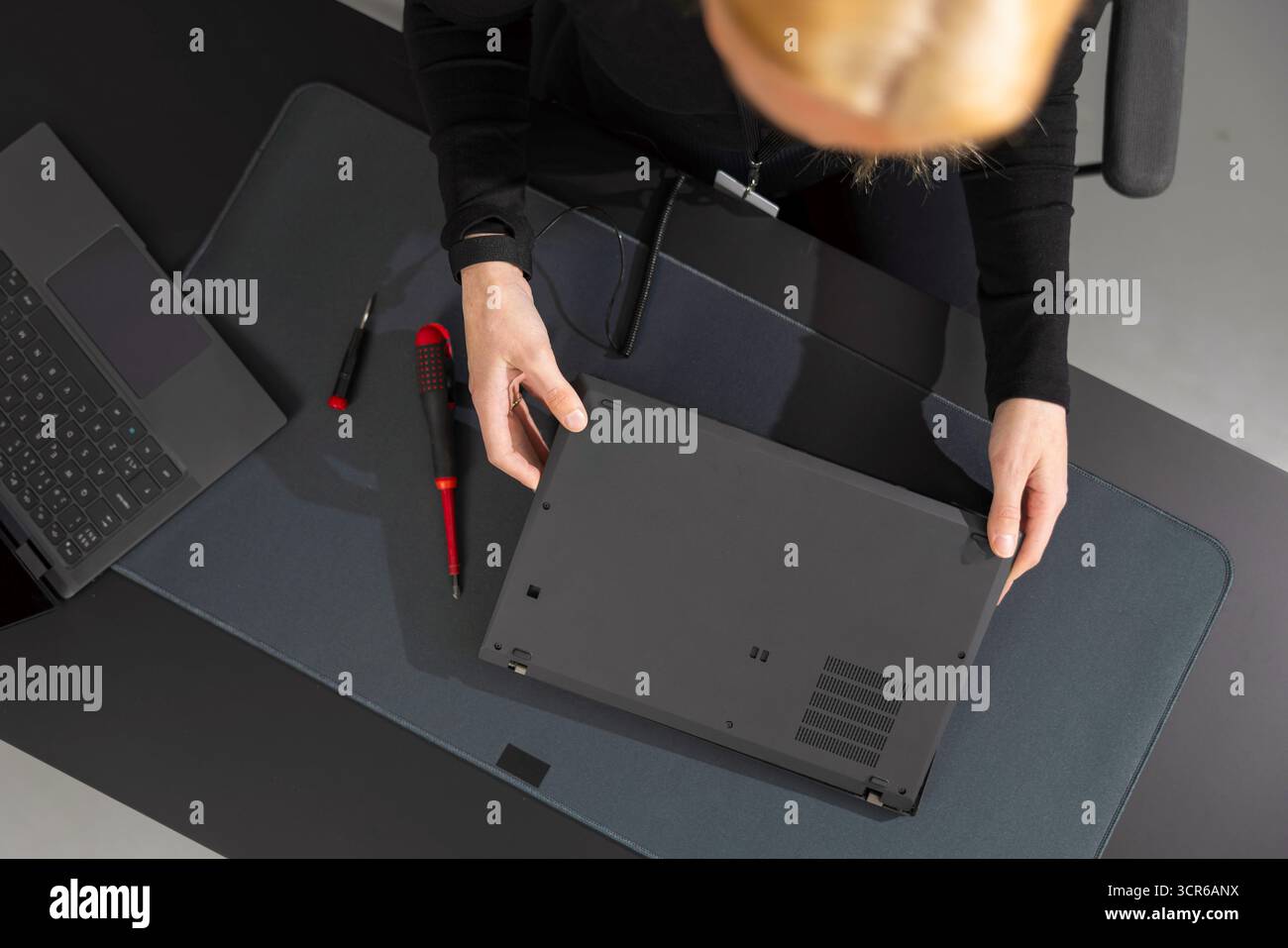 Eine IT-Technikerin in ihren 30ern repariert den Laptop an einem dunklen Schreibtisch mit Werkzeugen in der Nähe Stockfoto