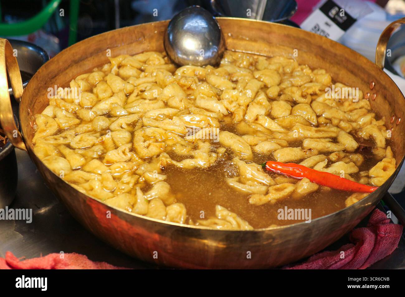 Geschmorte Fischsuppe in goldener Messingpfanne, authentisches thailändisches Streetfood mit reichhaltiger dunkler Brühe und scharfer Beilage, heiß und verzehrfertig serviert. Stockfoto
