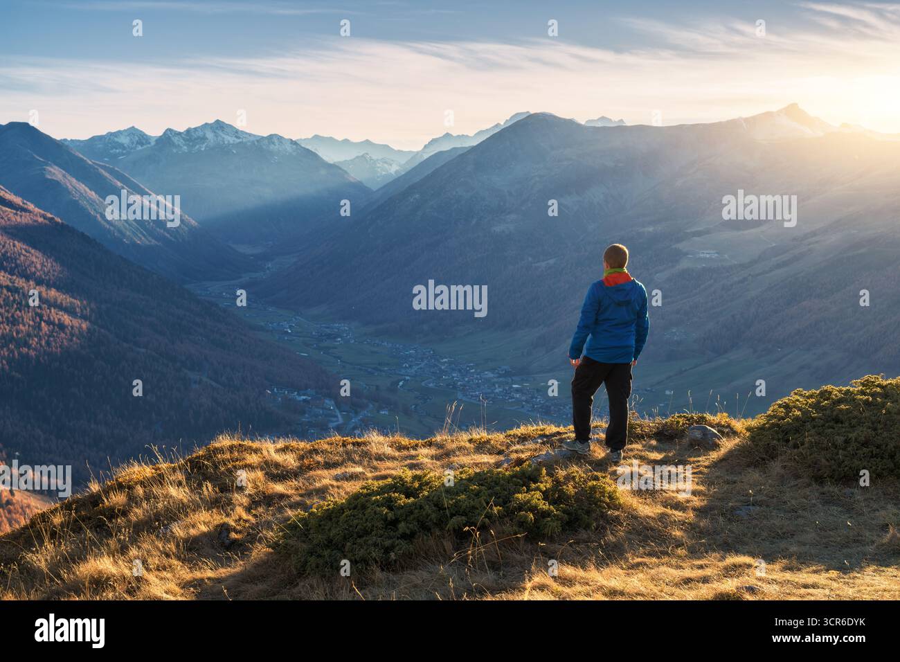 Junger Mann, der auf einem grasbewachsenen Bergrücken mit Blick auf das Tal steht Stockfoto