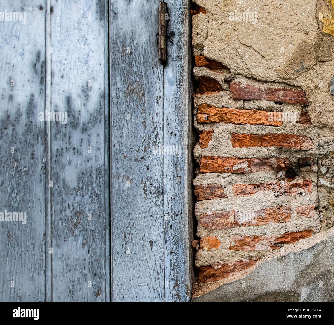 Rustikale alte Wand mit abblätterndem Putz, freiliegenden roten Ziegeln und verblasster antiker Tür. Perfekter strukturierter Hintergrund mit Kopierraum. Stockfoto