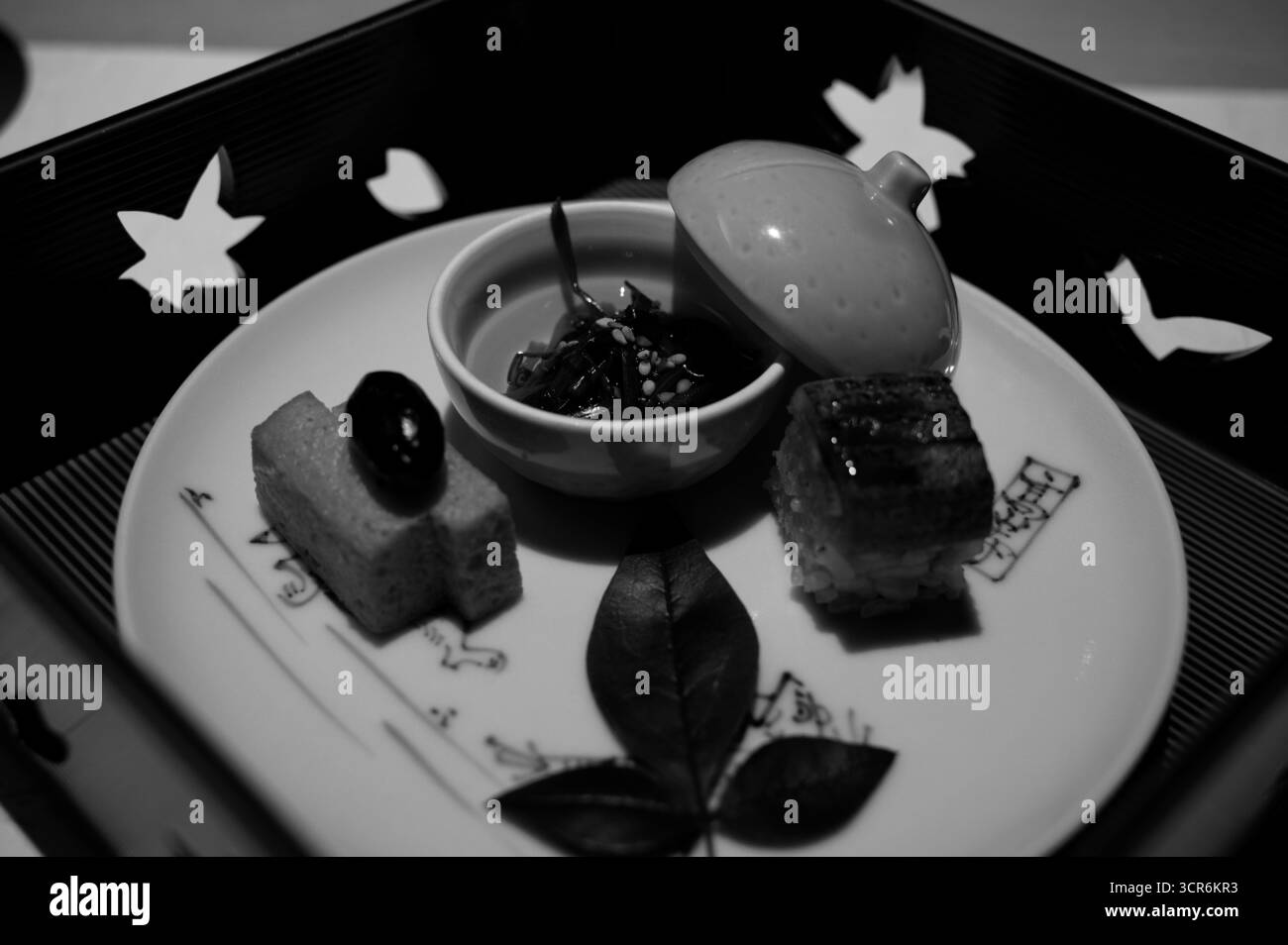 Elegante Kaiseki-Vorspeise mit Tamagoyaki, Aal-Sushi und Gemüse, serviert in einem delikaten Schwarzweiß-Gericht Stockfoto