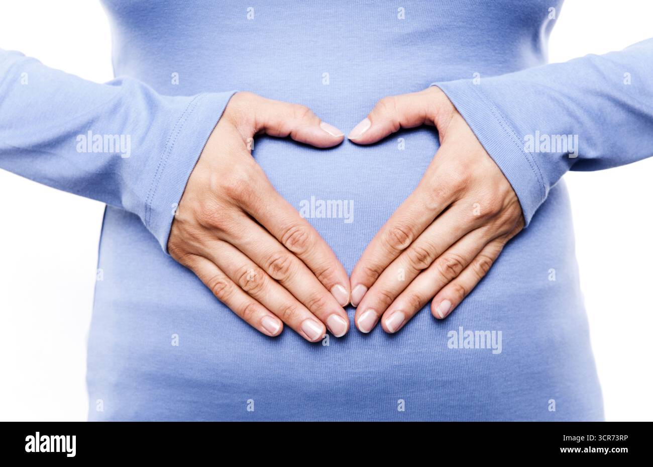 Hände, die ein Herz vor einer Babypuppe bilden, Vorfreude auf das Baby Stockfoto