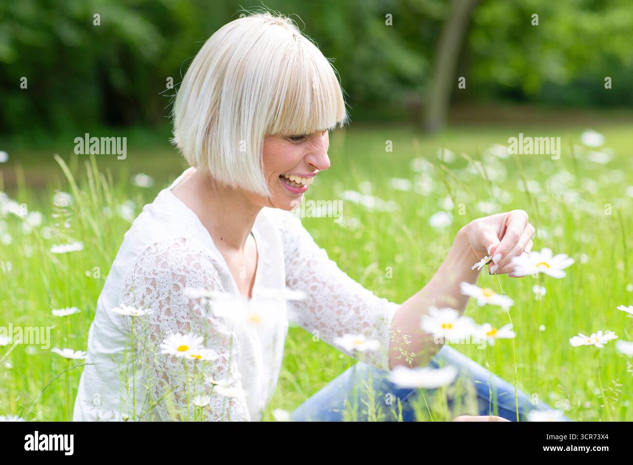 Glückliche Frau, die auf einer Wiese sitzt und ein Gänseblümchen in der Hand hält Stockfoto
