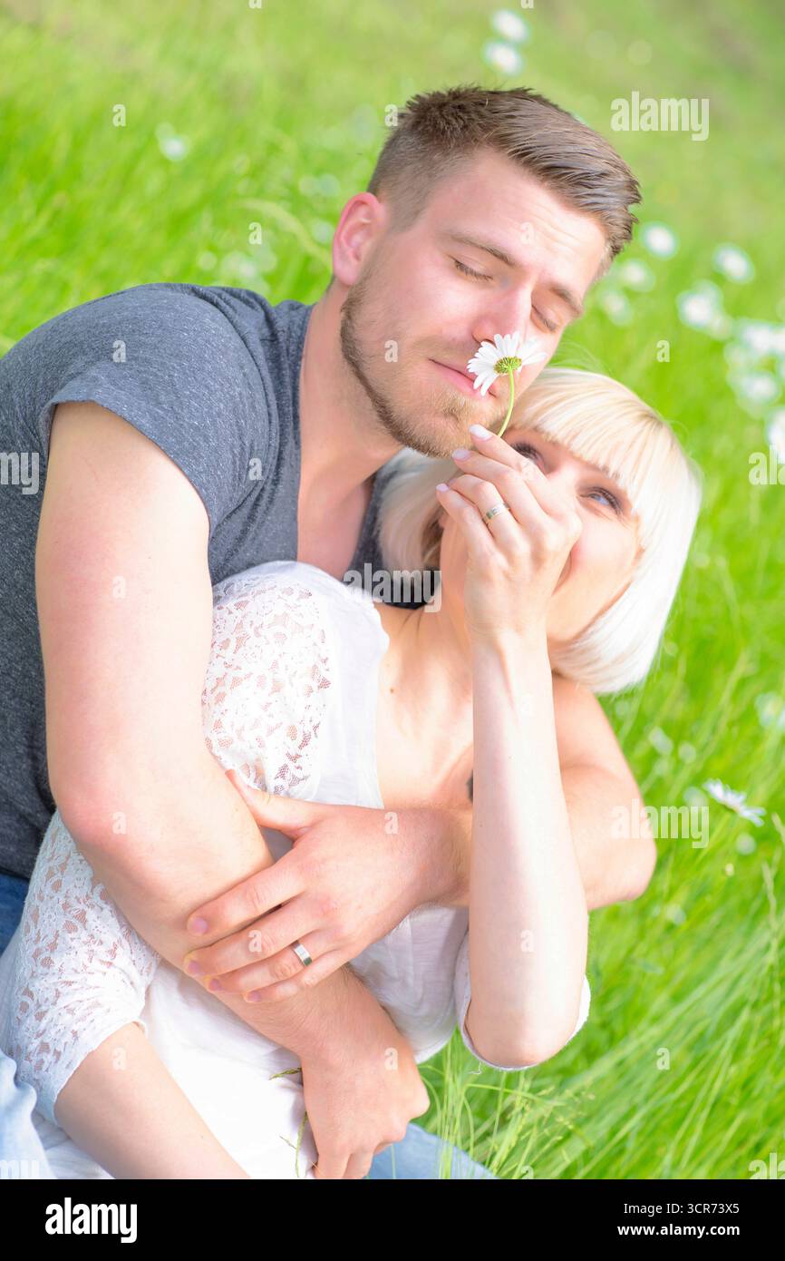 Ein verliebtes Paar sitzt auf einer Wiese und lässt ihn eine Blume riechen. Stockfoto