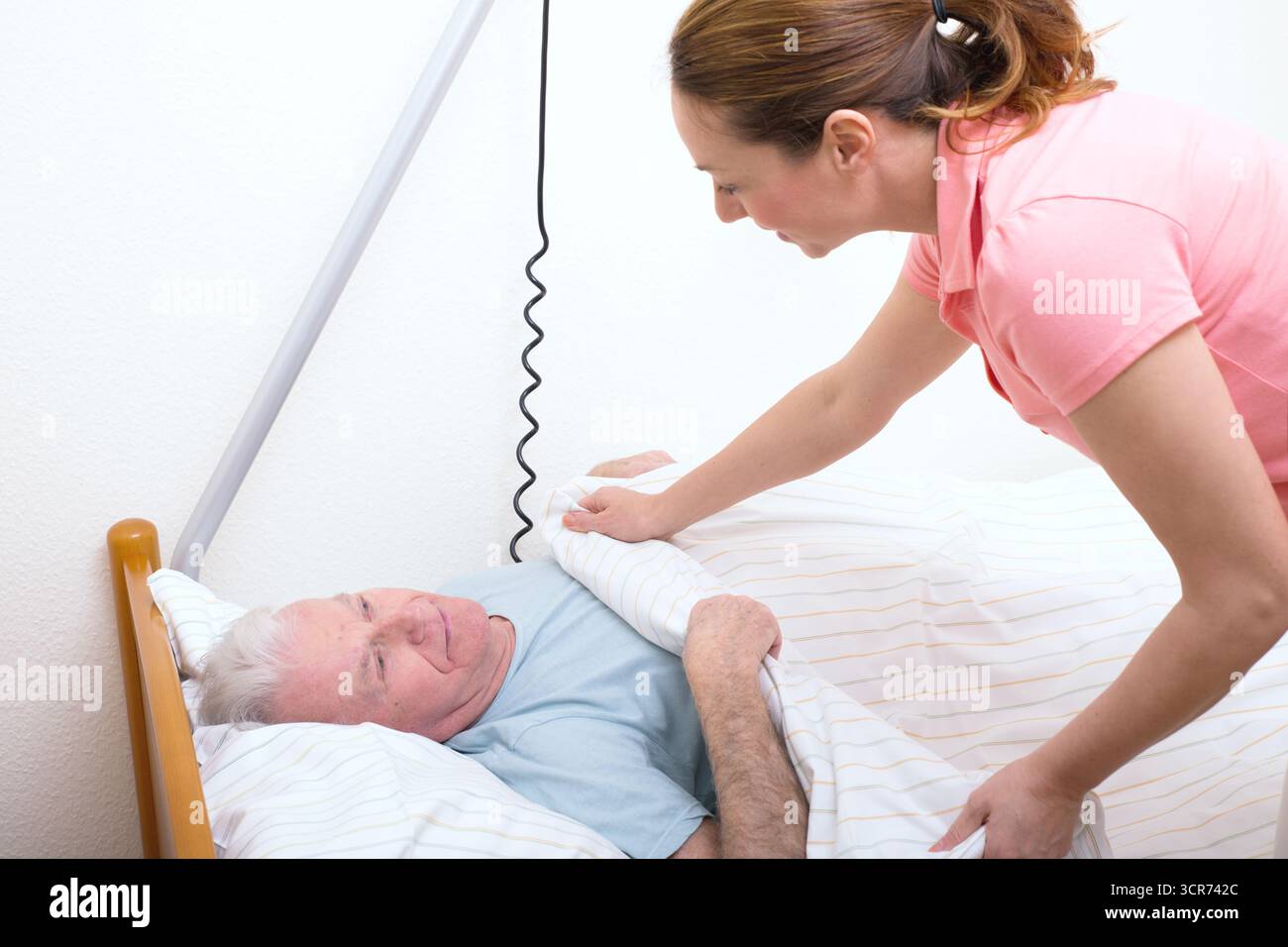 Senior im Pflegeheim im Bett, Krankenschwester deckt ihn ab Stockfoto