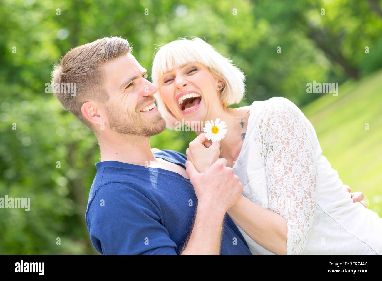 Ein verliebtes Paar steht überschwänglich auf einer Wiese mit Gänseblümchen in den Händen Stockfoto