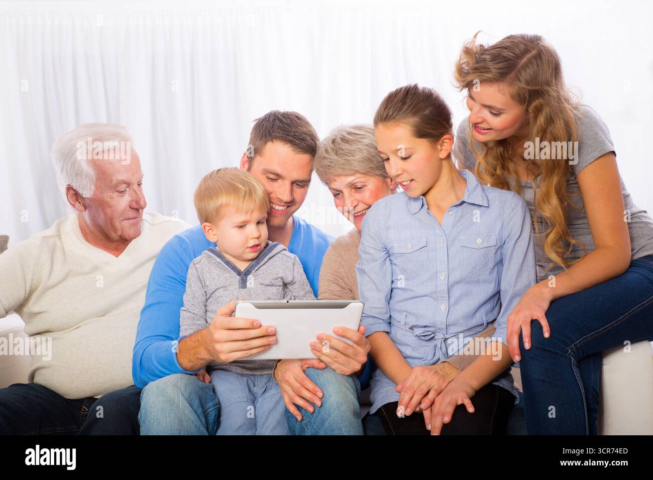 Familie mit zwo-Kindern, Oma und Opa auf dem Sofa, die zusammen ein Tablet sehen Stockfoto