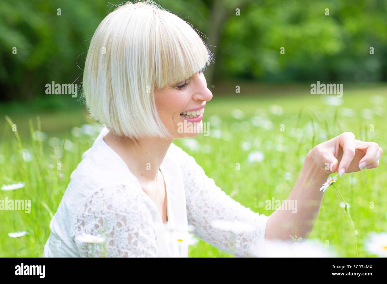Glückliche Frau, die auf einer Wiese sitzt und ein Gänseblümchen in der Hand hält Stockfoto