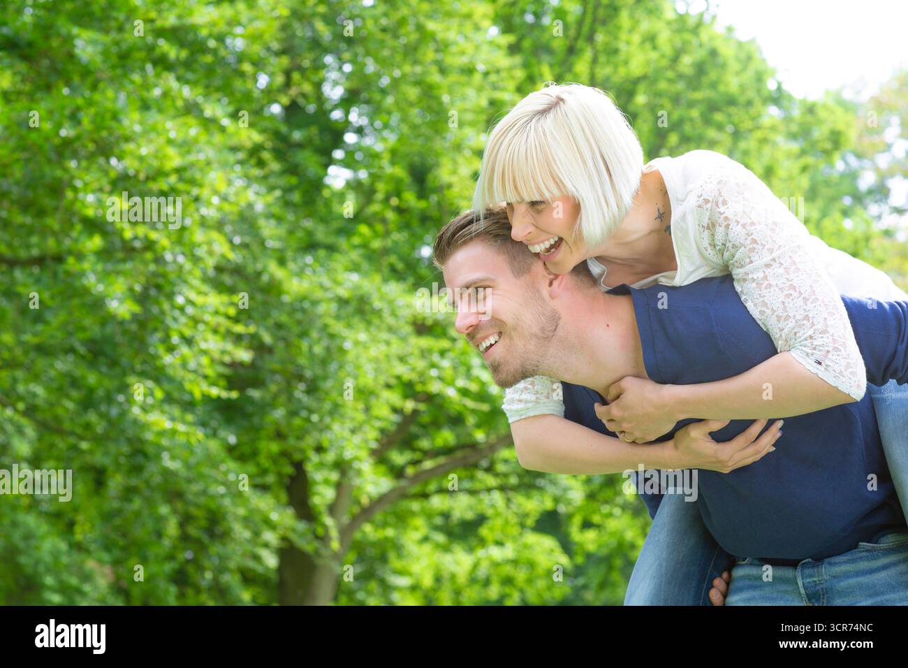 Ein junges, verliebtes Paar auf einer Wiese, er trägt ihr Huckepack Stockfoto