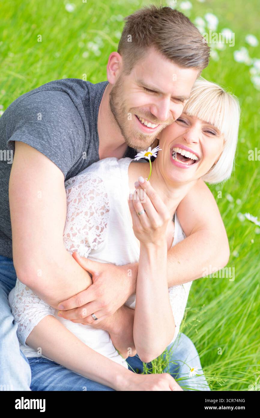 Ein verliebtes Paar sitzt glücklich auf einer Wiese mit Gänseblümchen. Stockfoto