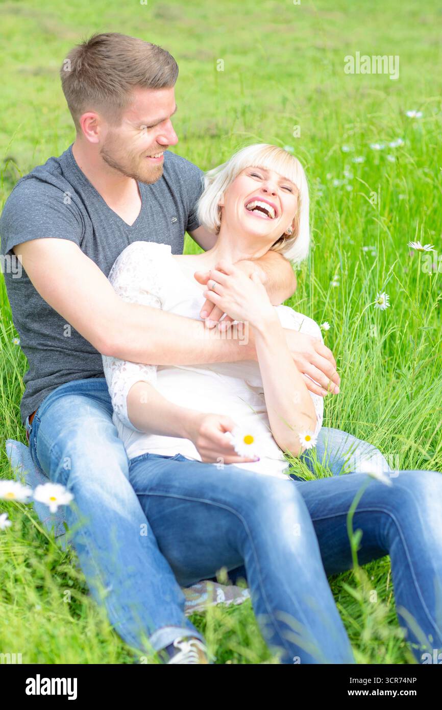 Ein verliebtes Paar sitzt glücklich auf einer Wiese mit Gänseblümchen. Stockfoto