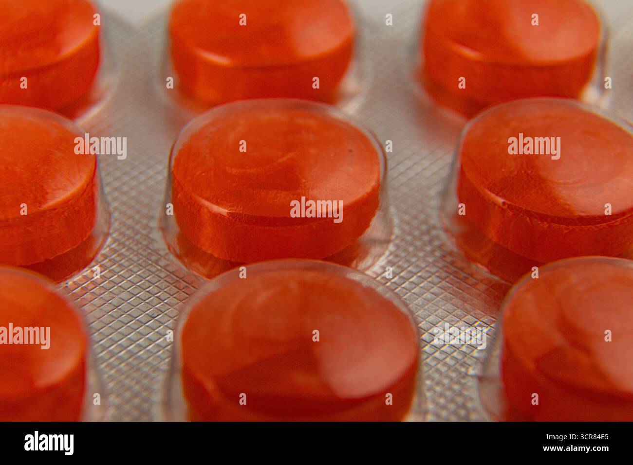 Nahaufnahme der roten runden Tabletten, die in einer Blisterpackung ordentlich angeordnet sind. Die glänzende Oberfläche reflektiert das Licht und zeigt ihre leuchtenden Farben und Glanz Stockfoto