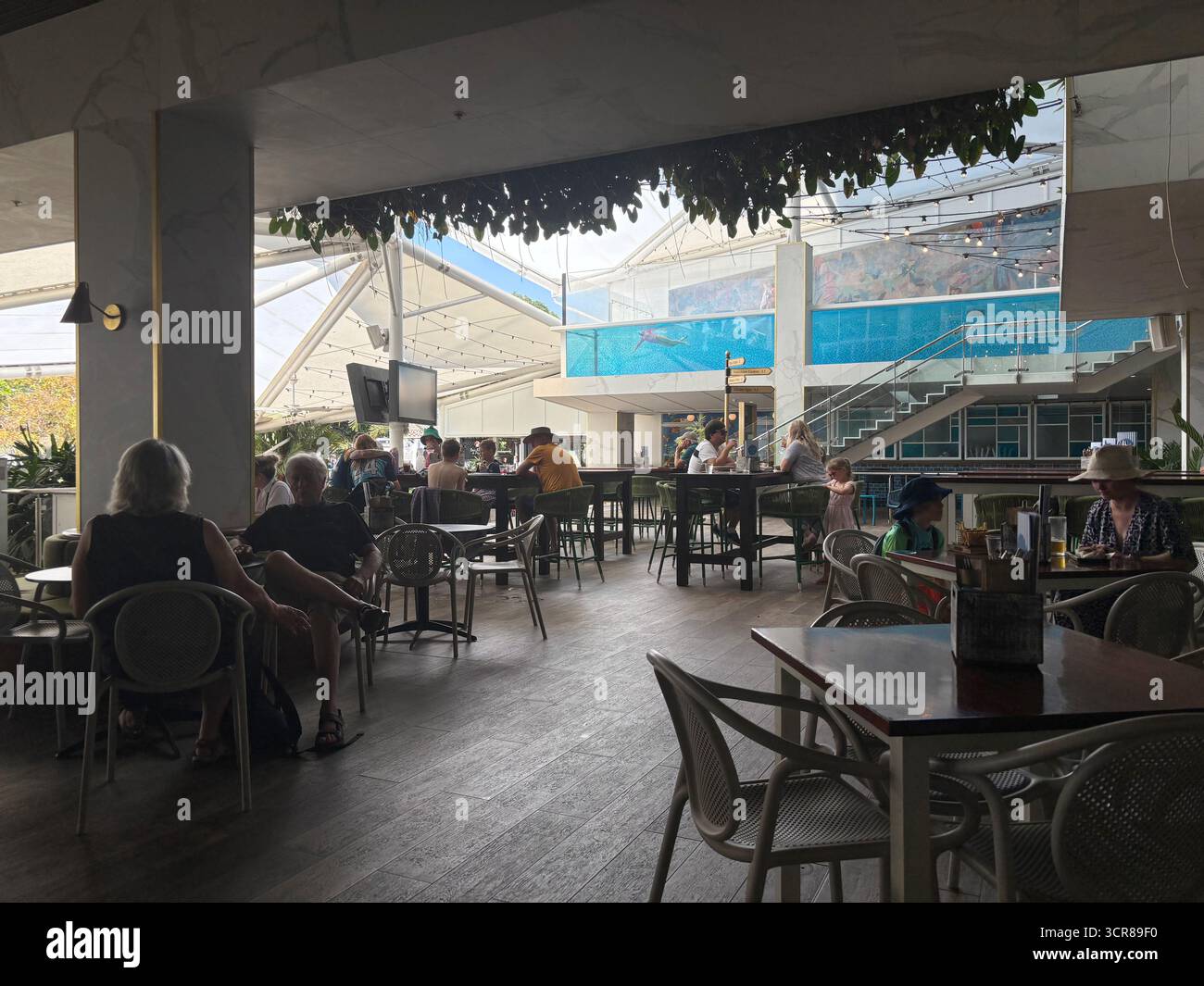 Leute essen und trinken im Boardwalk Social Restaurant, mit Schwimmer im Pool, Crystalbrook Flynn, Cairns, Queensland, Australien. Kein MR oder PR - Smartphone-aufgenommenes Stockfoto