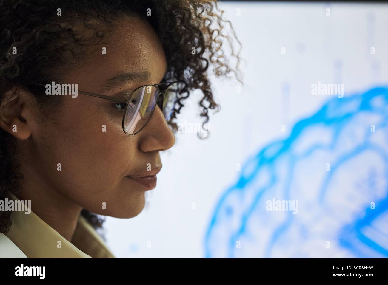 Junge Schwarze Frau mit Brille, die auf einer medizinischen Konferenz steht und sich auf die digitale Gehirnillustration konzentriert, die auf dem Bildschirm angezeigt wird, um das wissenschaftliche Forschungskonzept zu demonstrieren Stockfoto