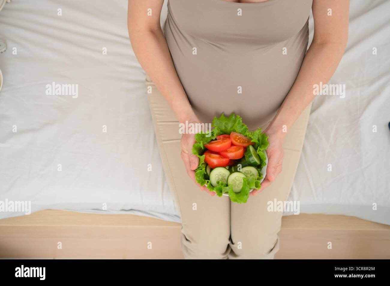 Eine heitere Mutter, die nahrhafte Gemüseplatte hält, während sie sich mit ihrem Baby anschließt. Ein nahrhafter Moment der Selbstfürsorge und mütterlichen Liebe. Stockfoto