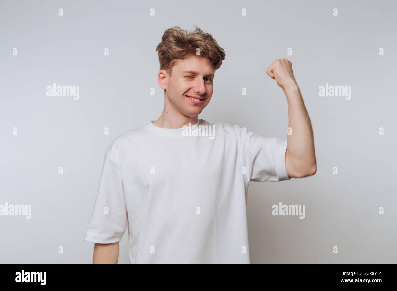 Junger Mann zeigt Stärke und Selbstvertrauen, während er vor einem einfachen Hintergrund zwinkert Stockfoto