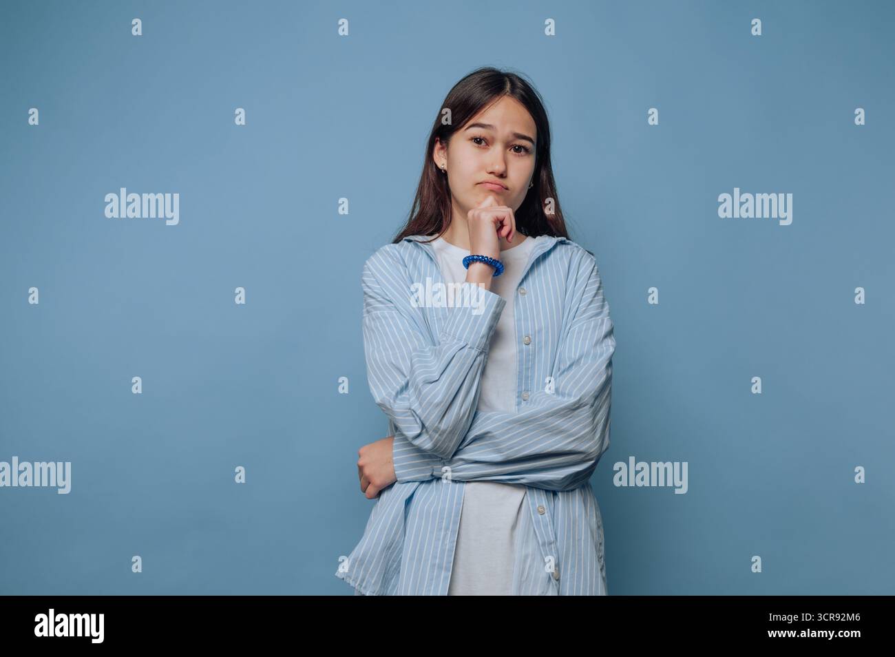 Nachdenkliche junge Frau zeigt einen kontemplativen Ausdruck auf hellblauem Hintergrund Stockfoto