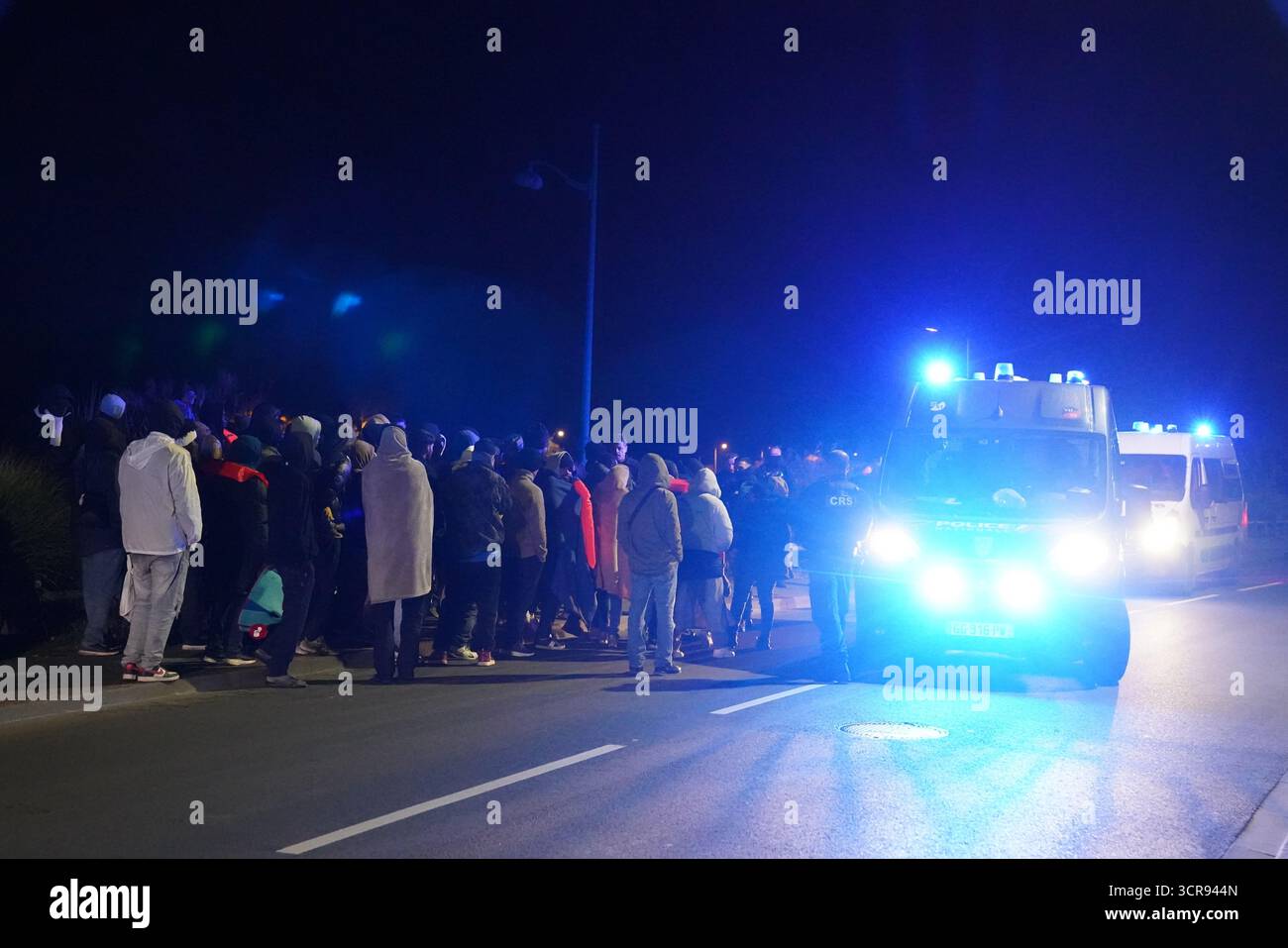 Französische Polizeibeamte eskortieren eine Gruppe von Menschen in der Nähe eines Kanals in Gravelines, Frankreich, wo Migranten versuchen, an Bord eines kleinen Bootes zu gehen, um den Ärmelkanal zu überqueren. Bilddatum: Dienstag, 30. September 2025. Stockfoto