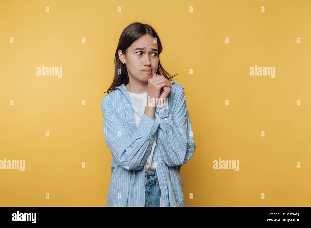 Eine junge Frau erscheint tief in Gedanken, ihr Verhalten reflektiert Reflexion und Rücksicht vor einem hellgelben Hintergrund. Stockfoto