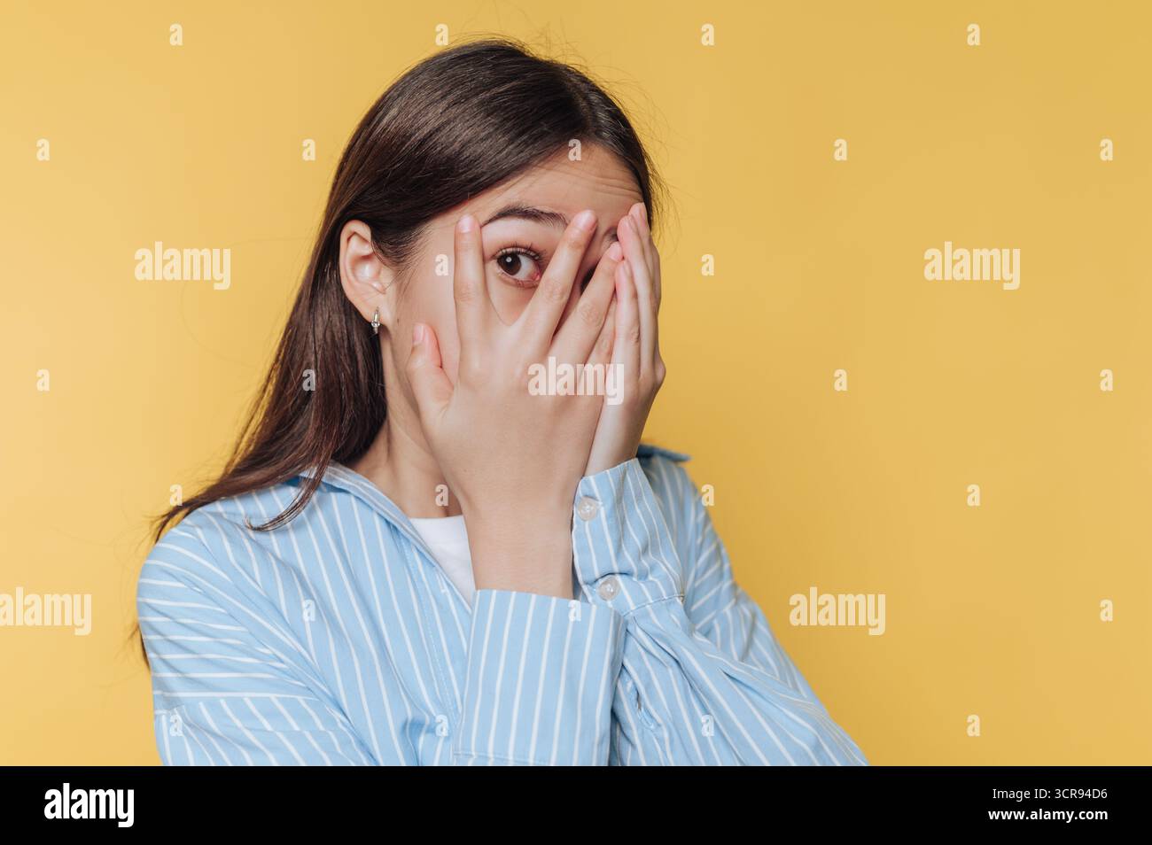 Die Frau bedeckt ihr Gesicht mit ihren Händen und drückt Angst und Unwohlsein auf leuchtend gelbem Hintergrund aus Stockfoto